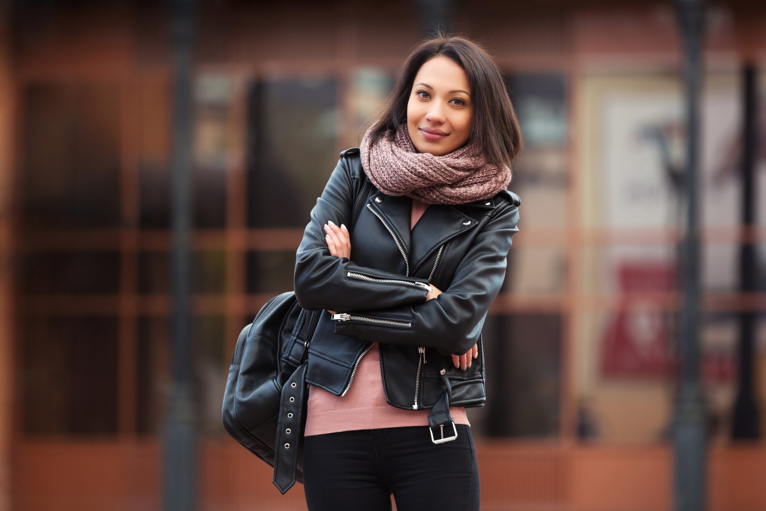 Young fashion woman with backpack walking in city street Stylish female model in black leather jacket outdoor